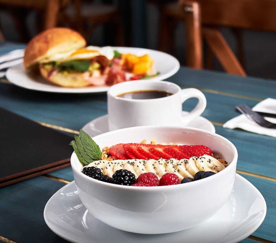 A breakfast setting with a bowl of fruit salad, a cup of coffee, and a sandwich on a table.