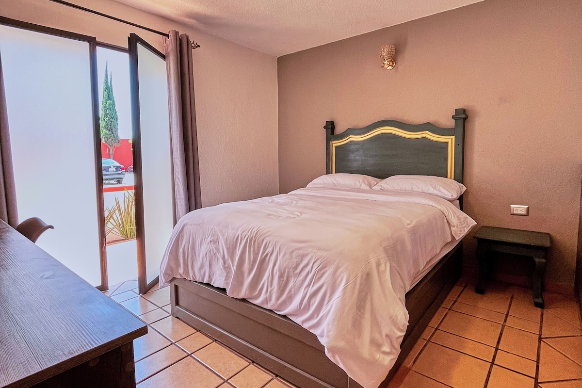 A bedroom with a bed, a small bedside table, and a chair.