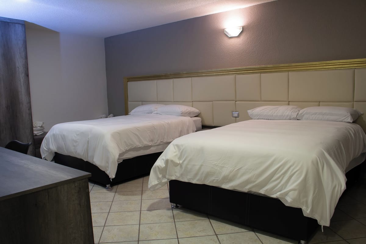 A hotel room with two beds, a desk, and a wall-mounted light fixture.