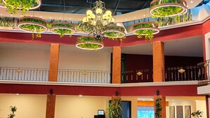 Un espacio interior amplio con varias mesas y sillas de comedor, una araña y adornos circulares en el techo con plantas.
