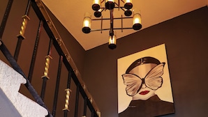 A staircase with a black and gold railing, a chandelier, and a framed artwork on the wall. - Hotel Casa Real  (San Andrés Cholula)