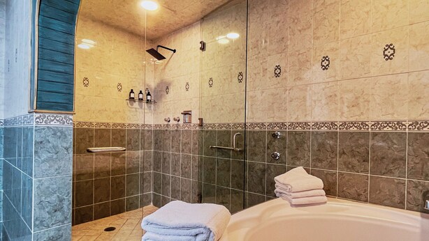 Un baño moderno con una bañera grande, zona de ducha y tocador con puertas de cristal.