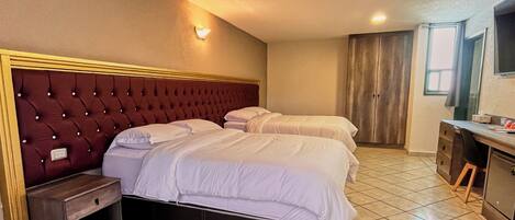 Habitación de hotel con dos camas, una mesita de noche de madera, un escritorio con silla y un televisor.