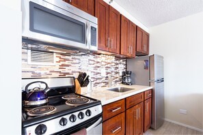 A kitchen with wooden cabinets, a stainless steel refrigerator, a microwave, a stove, and a tiled backsplash. - "Ali'i" Studio w/ FREE Parking & Full Kitchen (Honolulu)