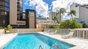 A swimming pool with a clear blue water, surrounded by lounge chairs and a white fence.