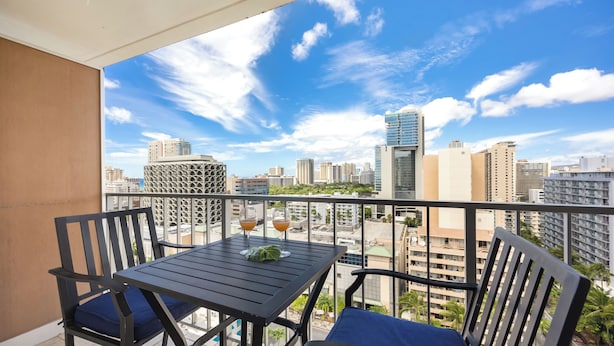 A balcony with a table and chairs, overlooking a cityscape with tall buildings.
