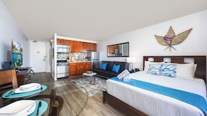 A hotel room with a bed, a sofa, a dining table, and a kitchen area.