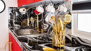 A kitchen with a black and white marble countertop, gold utensils, and red cabinets. - Hermosa Suites n the heart of Punta Cana (Punta Cana)