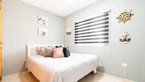 A bedroom with a bed, a window with blinds, and nautical-themed wall decor. - Hermosa Suites n the heart of Punta Cana (Punta Cana)