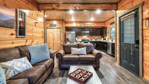 L’intérieur chaleureux d’un chalet comprend un salon avec un canapé en cuir marron et une table basse, une cuisine équipée d’appareils modernes et des murs en bois.