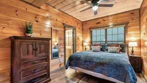 Une chambre dans une cabane en bois, avec un lit, une commode et un ventilateur de plafond.