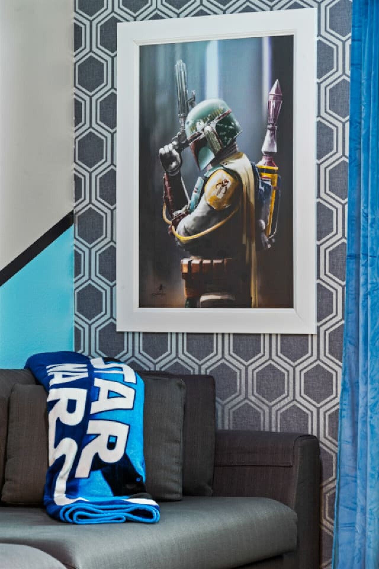 A framed artwork of a character in a helmet and armor, a grey sofa with a blue blanket, and a patterned wall.
