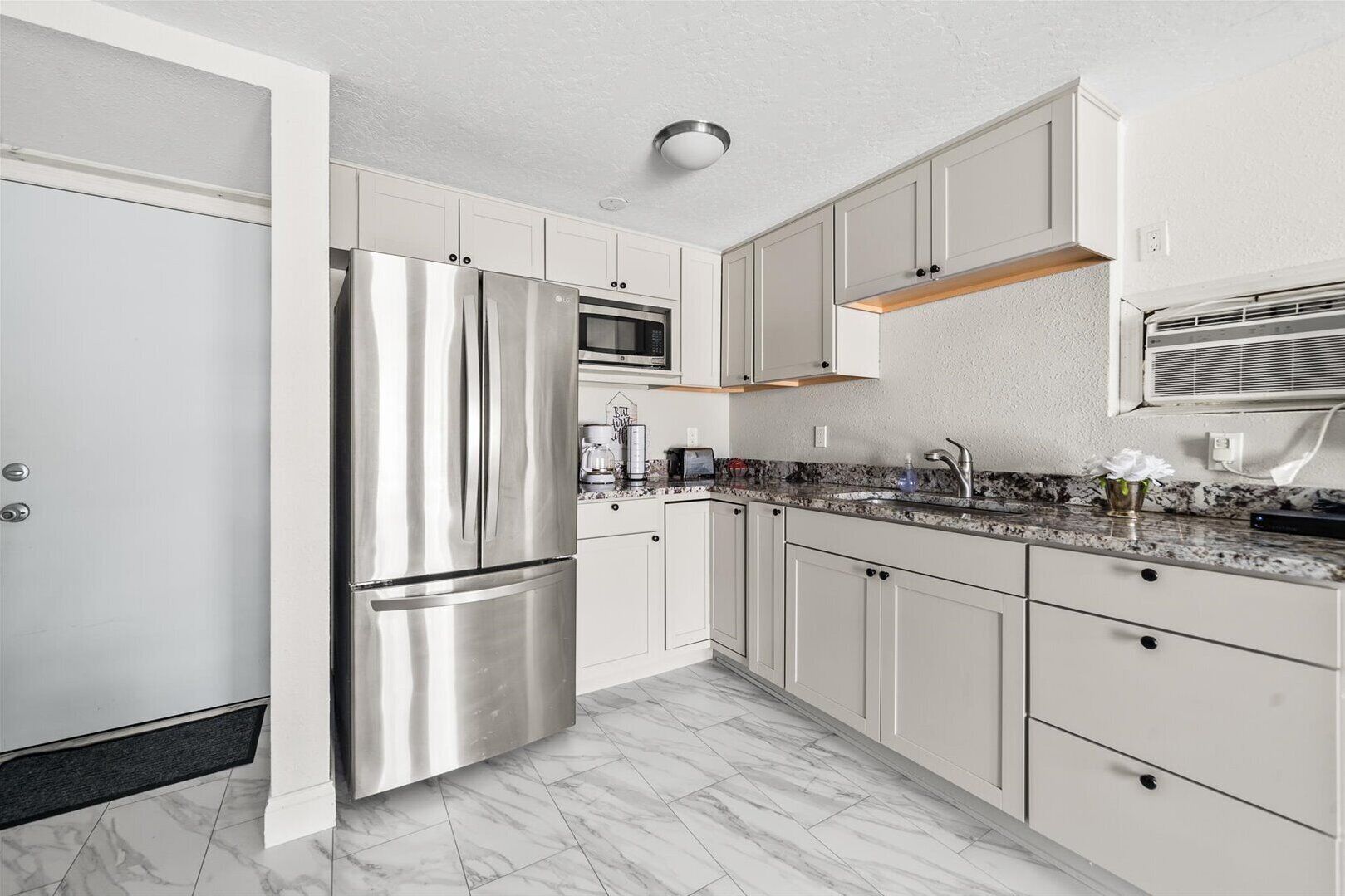 A modern kitchen with white cabinets, stainless steel appliances, and a marble floor.