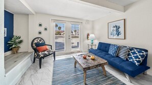 A living room with a blue sofa, a patterned armchair, a coffee table, and a door leading outside.