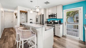 A modern kitchen with white cabinetry, a central island with bar stools, stainless steel appliances, and a teal accent wall.