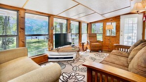 A cozy cabin interior with large windows, a fireplace, and a comfortable seating area.