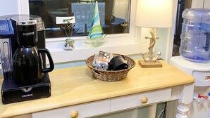 A kitchen counter with a coffee maker, a basket with a small figurine, a lamp, and a water dispenser.