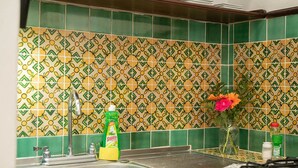 A kitchen with green and yellow patterned tiles, a stainless steel sink, and a vase with flowers on the counter. - Casita La Pila (Antigua Guatemala)