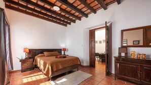 A bedroom with a bed, wooden headboard, a nightstand with a lamp, a dresser, and a mirror. - Casita La Pila (Antigua Guatemala)