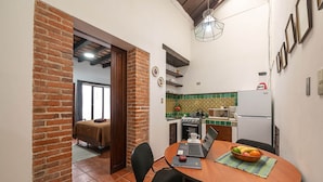 A compact kitchen with a dining area, featuring a brick wall, tiled backsplash, and a small refrigerator. - Casita La Pila (Antigua Guatemala)