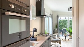 A modern kitchen with an oven, stove, and range hood. There is a dining area with a chair and a table, and a view of a garden through large windows. - 2 bedroom stunning home in Heinkenszand (Heinkenszand)