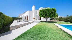 Ein modernes Haus mit Swimmingpool, einer Steinterrasse und einem gepflegten Rasen.