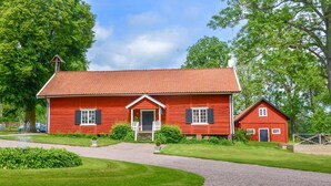 Une maison en bois rouge avec un toit en tuiles, un porche à l’avant et un petit bâtiment attenant.