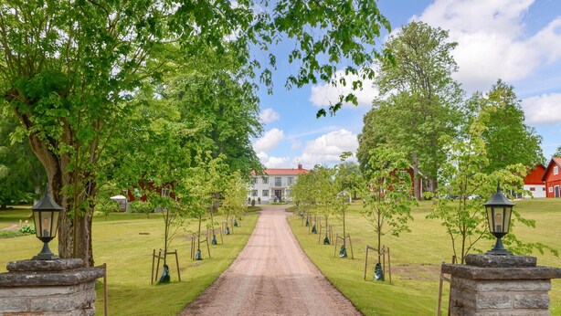 Un chemin de gravier mène à un bâtiment doté d’un toit rouge, entouré d’arbres et de lampadaires en pierre.