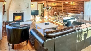Un intérieur chaleureux de chalet en bois, avec une cheminée, des canapés en cuir, un coin repas et un téléviseur.