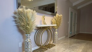 A hallway with a marble floor, a large mirror, a gold-framed console table, two decorative vases with pampas grass, and a chandelier. - Newly Remodeled 4 bedroom House (Lancaster)