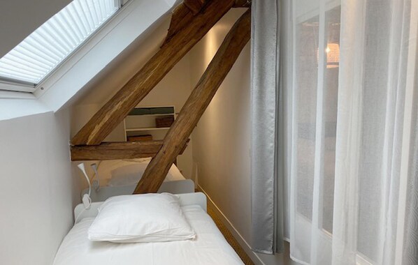 A small, single-bed room with a sloped ceiling, a skylight, and a window with sheer curtains. - Amazing home in Flacy with WiFi (Flacy)
