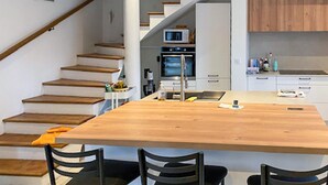 Una cocina moderna con una isla de madera, electrodomésticos integrados y una escalera que sube a otro nivel.