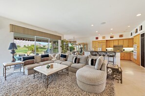 A spacious living room with a large sectional sofa, a coffee table, and a view of the kitchen.