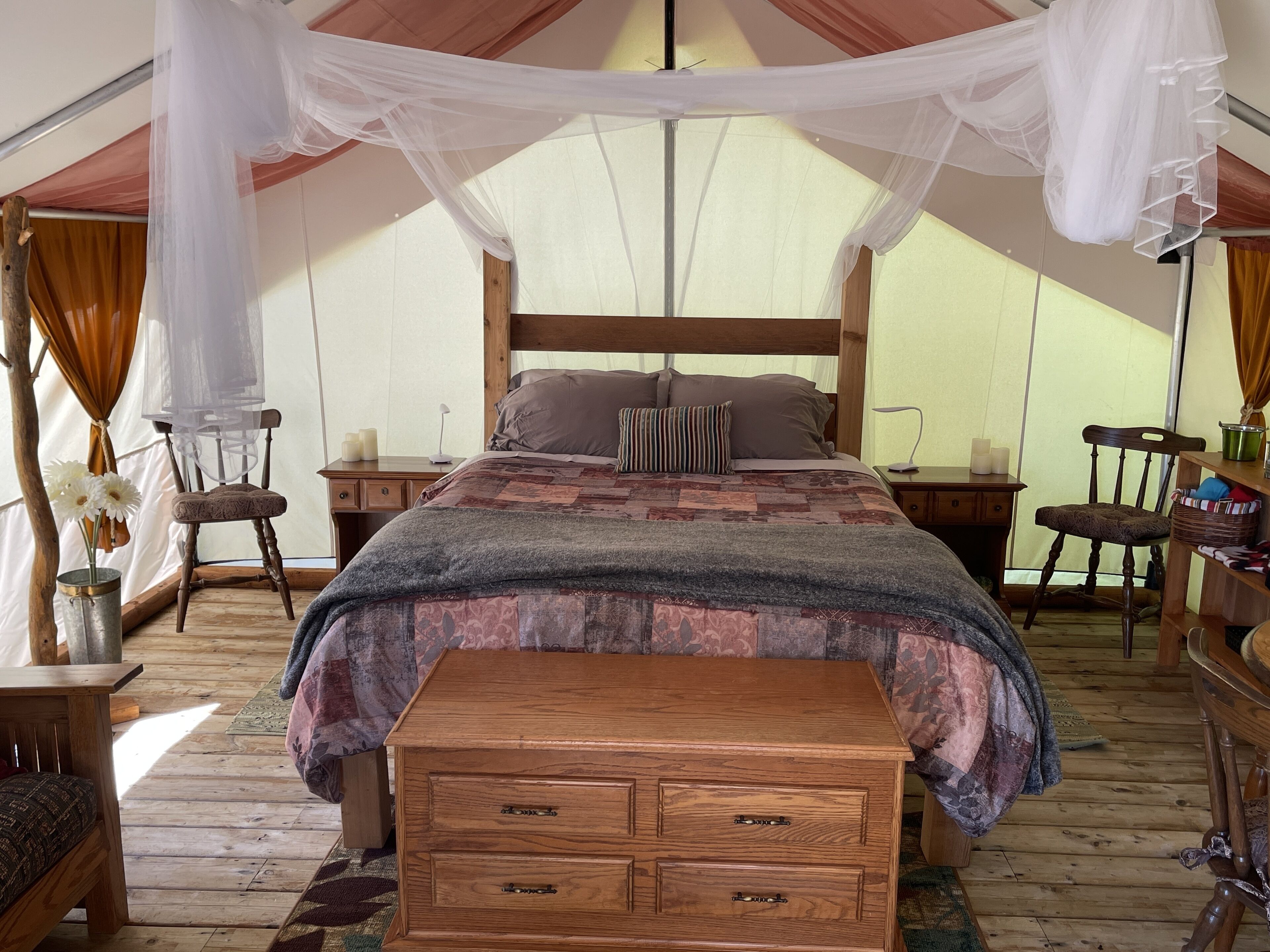 A tented accommodation with a wooden bed, a bench, and a nightstand with candles.