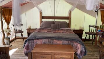 A tented accommodation with a wooden bed, a bench, and a nightstand with candles.