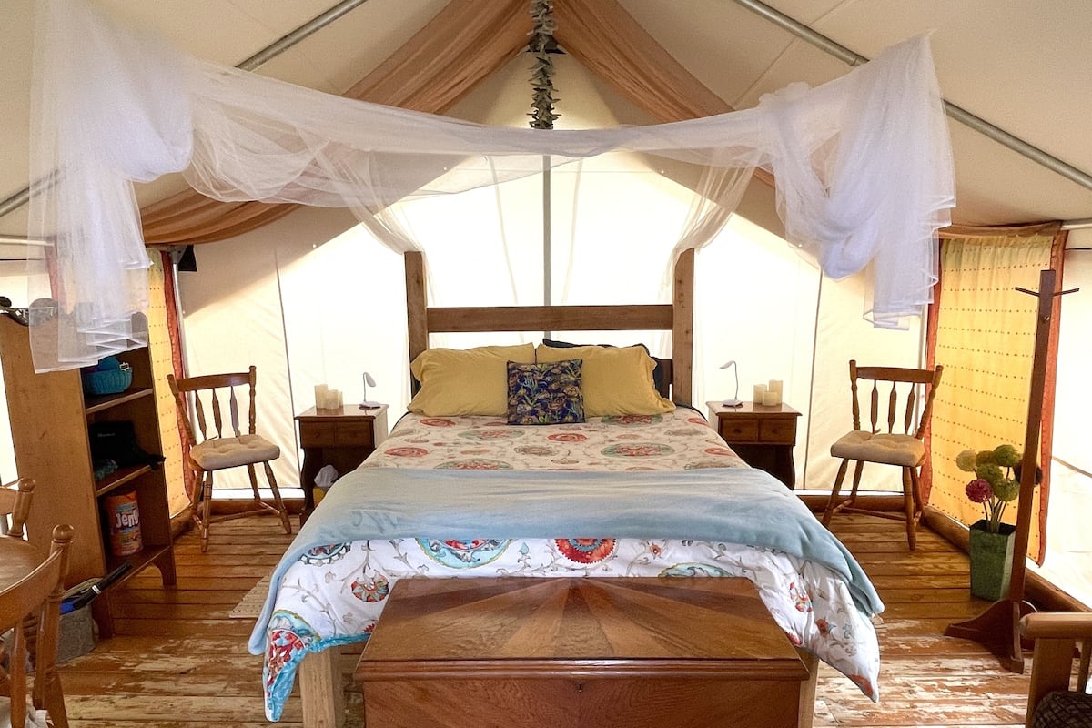 Un dormitorio tipo tienda de campaña con cama de madera, mesita de noche, silla y cómoda.