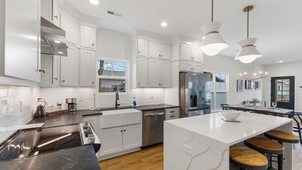 Una cocina moderna con armarios blancos, electrodomésticos de acero inoxidable y una isla central con taburetes.