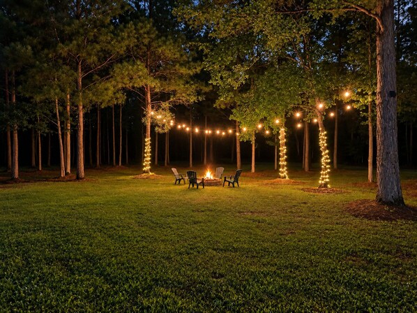 An outdoor seating area with chairs and a fire pit, surrounded by trees and string lights.