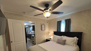 Een hotelkamer met een bed, een plafondventilator, een nachtkastje en een deur naar een badkamer.