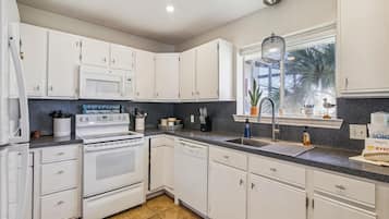A modern kitchen with white cabinets, a stainless steel sink, and a window with a view of palm trees.