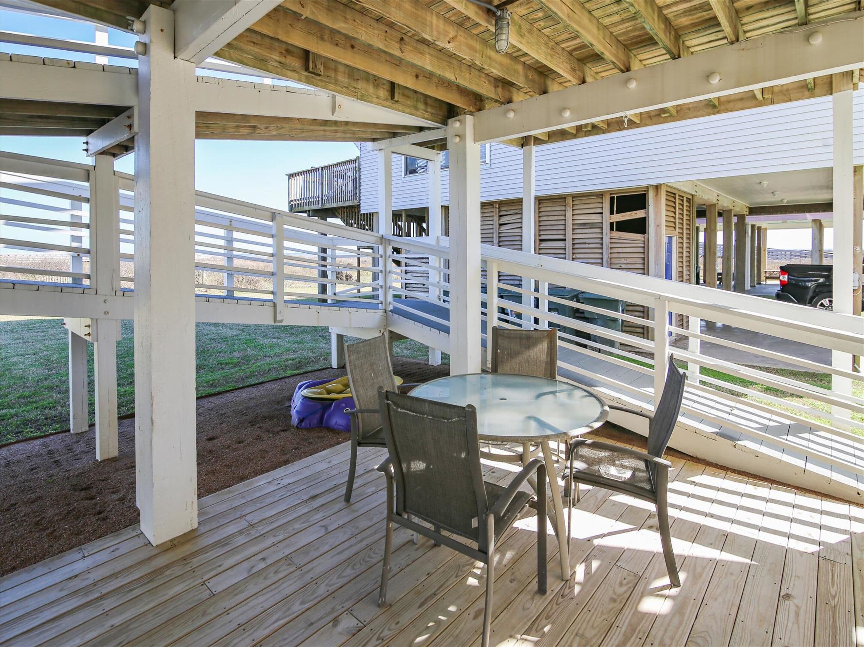 A covered outdoor patio with a table and chairs, wooden deck, and a view of a building with a balcony.