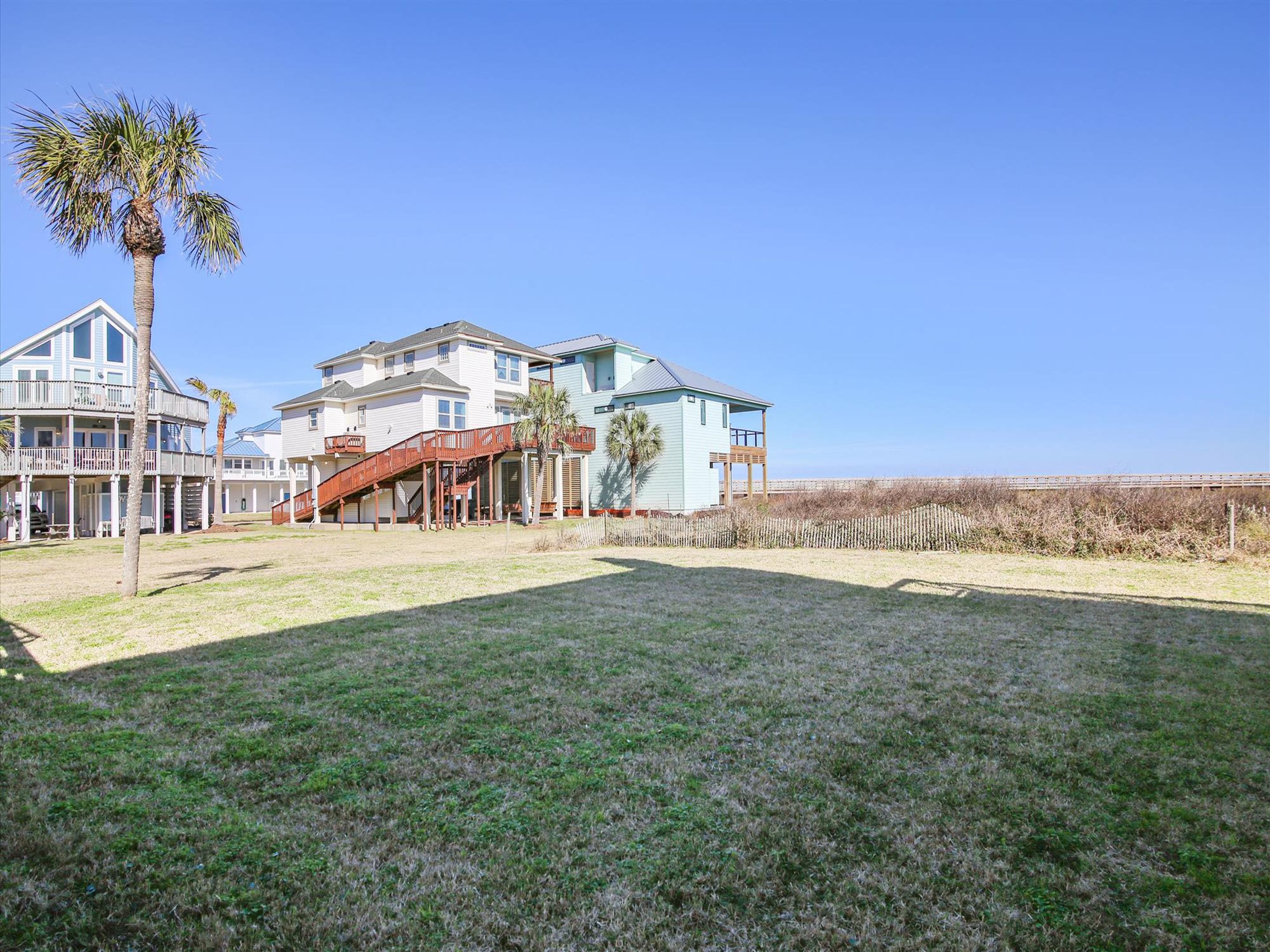 A beachfront property with a large house, a covered deck, and a grassy yard.
