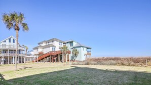 A beachfront property with a large house, a covered deck, and a grassy yard. - La Dolce Vita (Playa San Luis) by Ryson Vacation Rentals (Galveston)