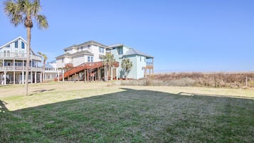 A beachfront property with a large house, a covered deck, and a grassy yard.
