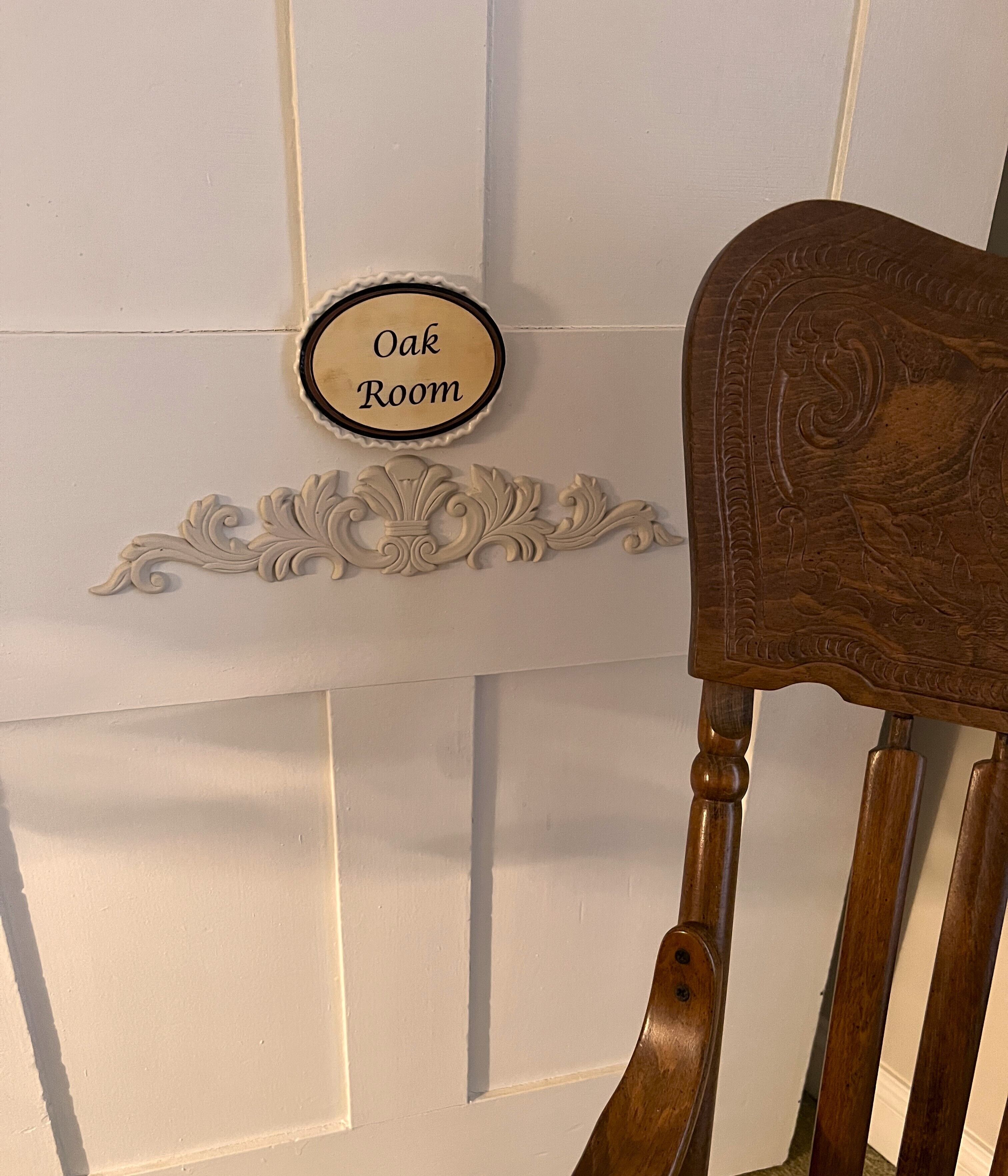 A wooden chair with a carved headrest and a sign above it that reads "Oak Room".
