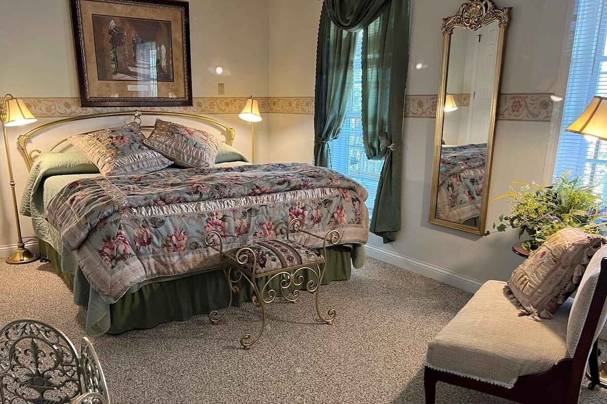 A bedroom with a bed, a chair, a mirror, and a picture on the wall.