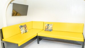 A yellow sectional sofa with two decorative pillows, a small rug, and a flat-screen TV mounted on the wall. - Cozy Nook nestled in the Santa Cruz Valley. 
Queen sized bed Hot and cold shower (Santa Cruz)