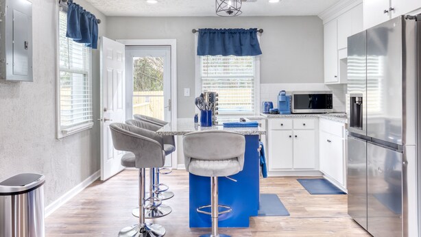 A modern kitchen with white cabinets, a stainless steel refrigerator, a blue island with bar stools, and a microwave. - Cozy Home with City Views (Columbus)