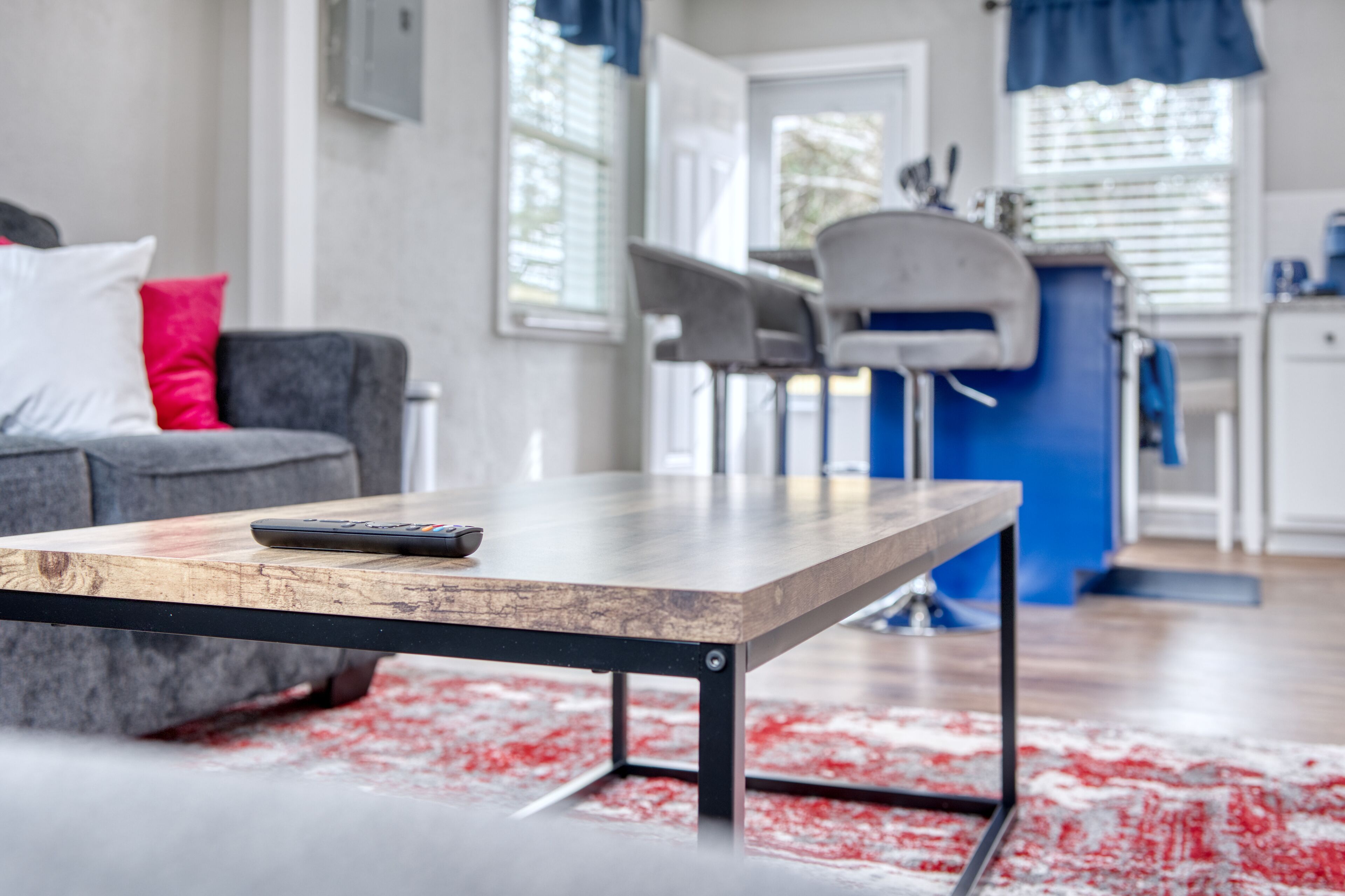Un salon moderne avec une table basse en bois, un canapé gris agrémenté de coussins rouges et un mur d’accent bleu.