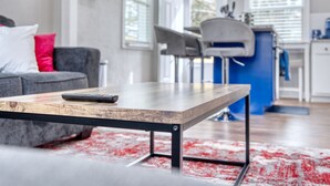 A modern living room with a wooden coffee table, a grey sofa with red cushions, and a blue accent wall. - Cozy Home with City Views (Columbus)